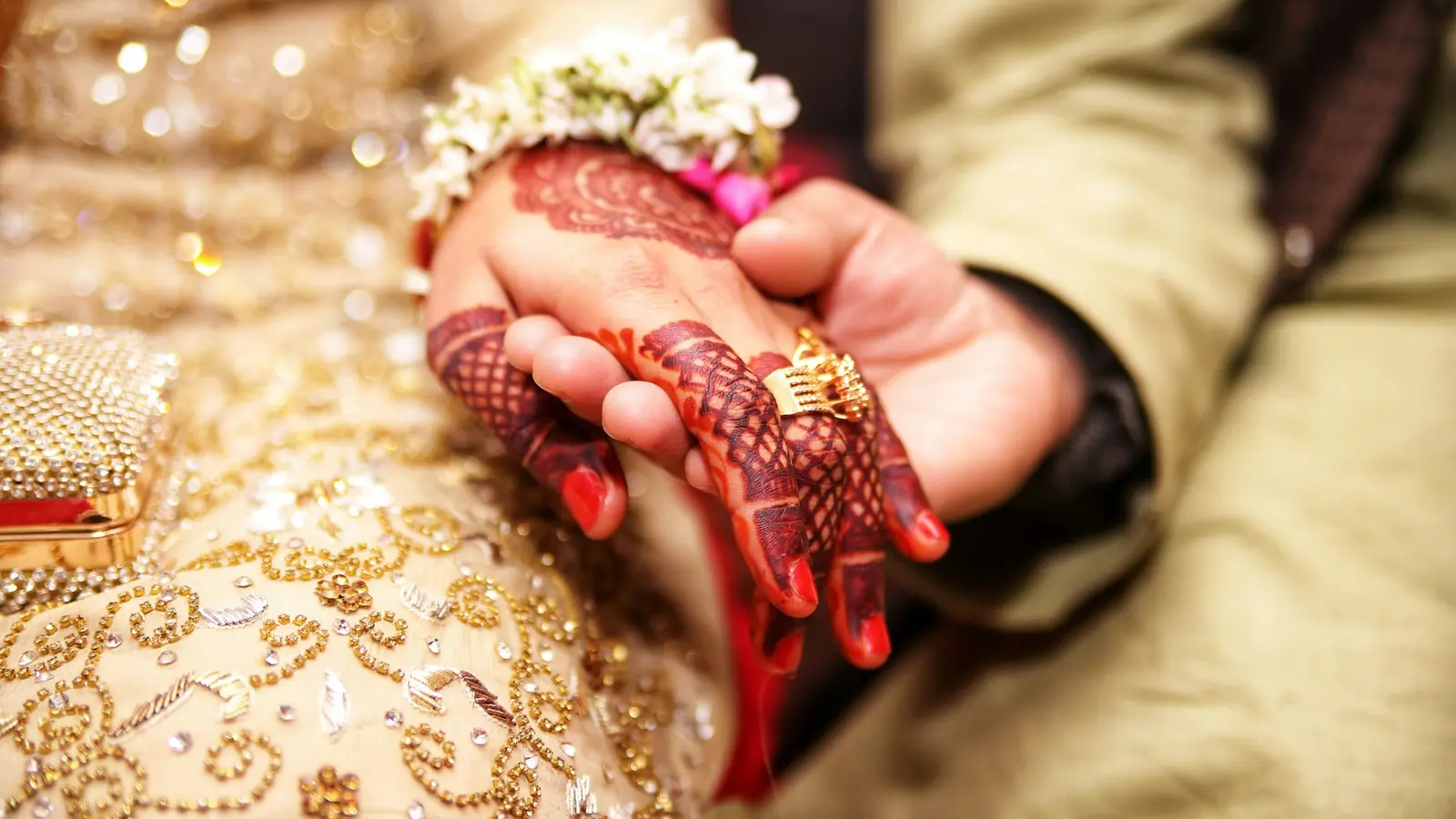 A bride’s hand painted with henna resting in the groom’s hand at their wedding.