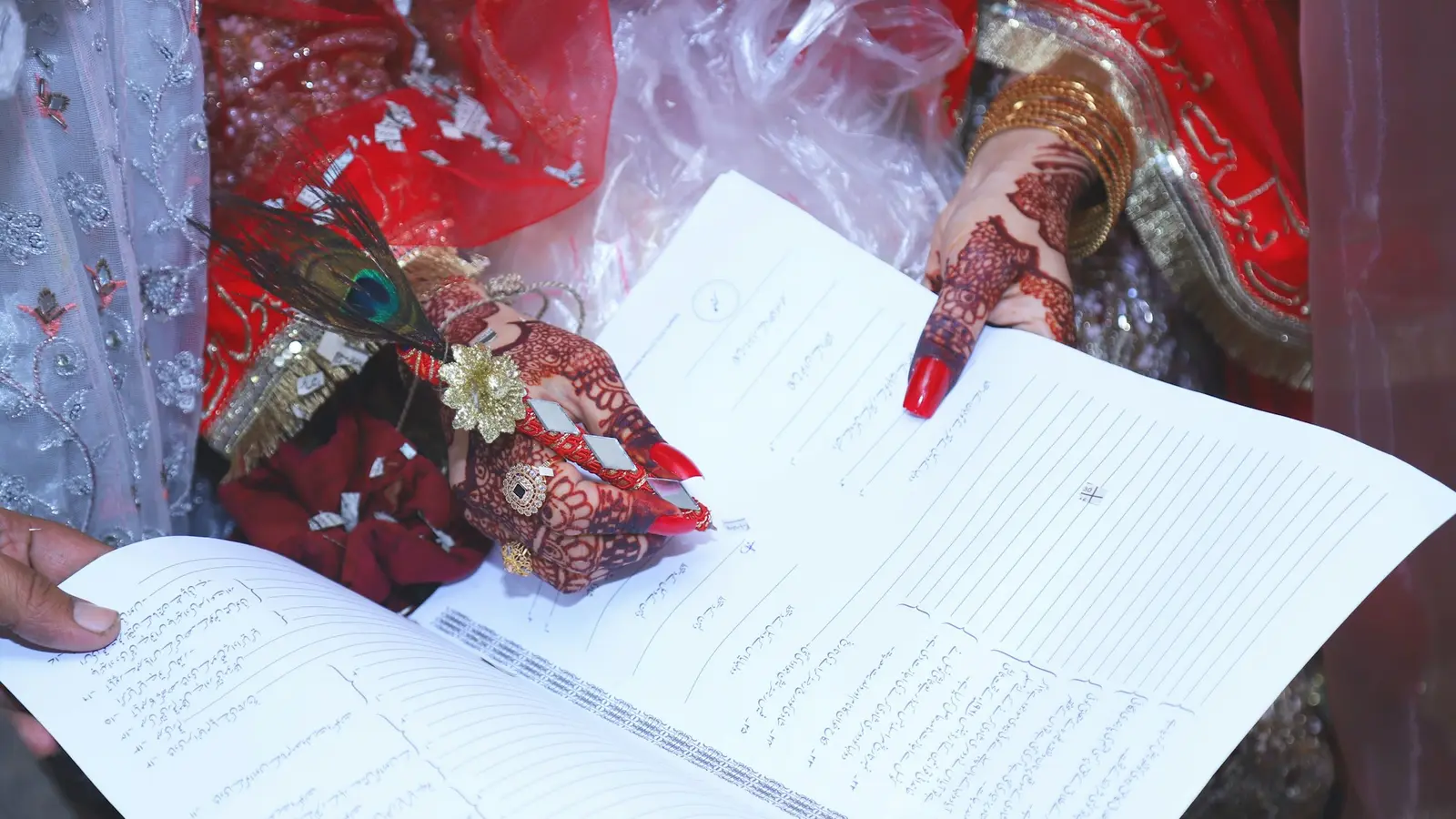 A bride with henna on her hands signing her nikah contract, the pages laid open in front of her.